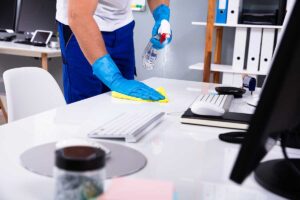 A person wearing gloves wipes a household light switch with a disinfectant cloth in a well-lit kitchen.