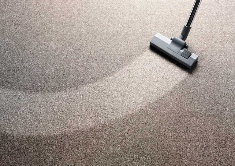 A person wearing gloves uses a squeegee to remove pet hair from a carpeted living room floor.