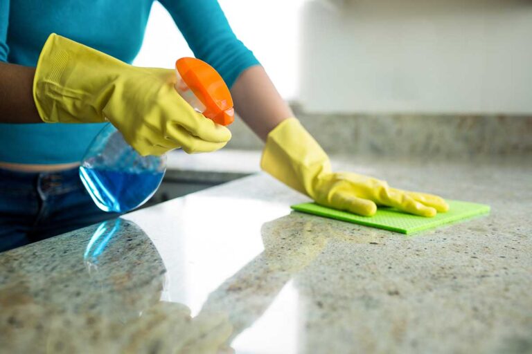 A parent cleaning a kitchen counter while a child and dog play nearby on the floor.