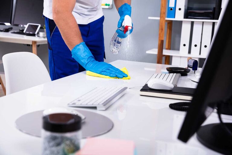 A person wearing gloves mixes natural cleaning ingredients in a glass bowl on a kitchen counter.