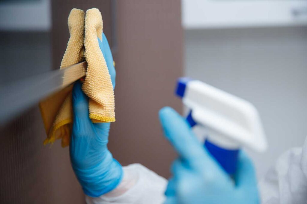 A person washes a sponge and dishcloth beside a kitchen sink before placing them on a drying rack.