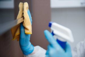 A person washes a sponge and dishcloth beside a kitchen sink before placing them on a drying rack.