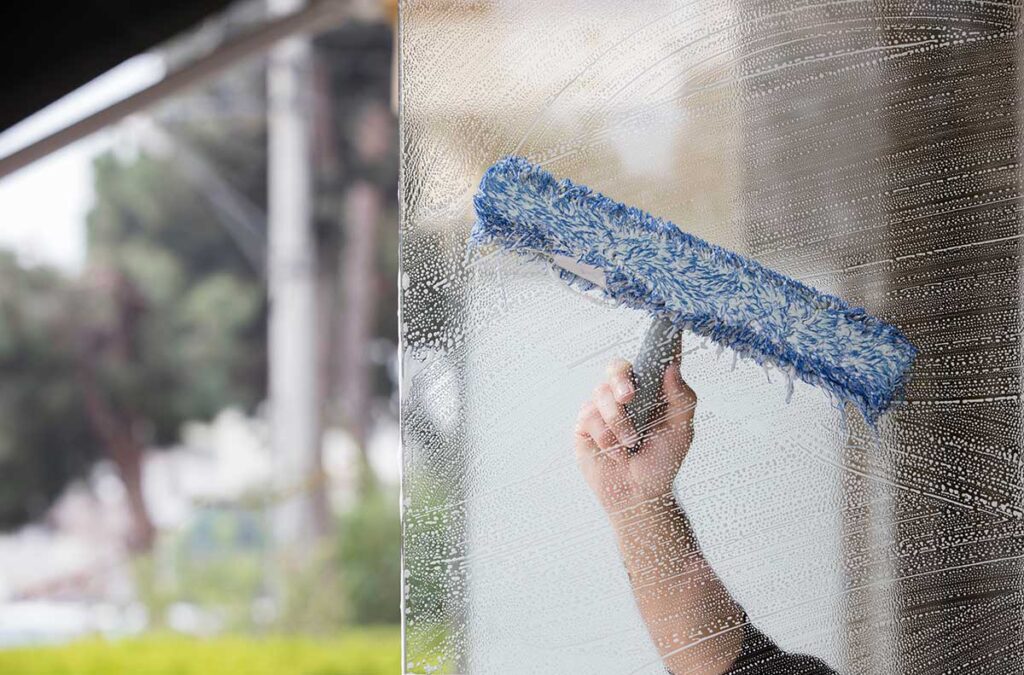Hands clean a dishwasher filter beside an open appliance with a soft brush and microfiber cloth.