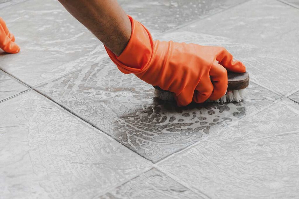 Person wiping shower tile with a squeegee beside a running bathroom exhaust fan.